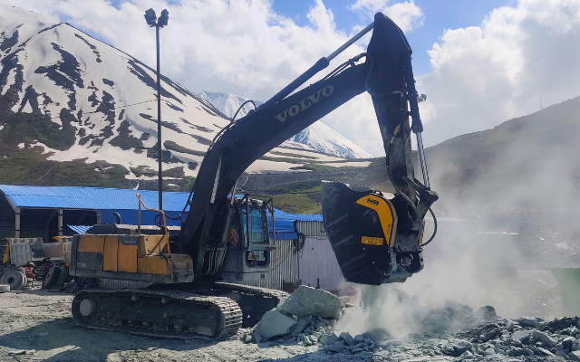 MB Crusher bucket efficiently processing river rock for road construction."